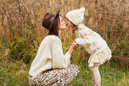 Sideview portrait of beautiful mother and daughter in fashionable autumn clothes  kissing each other...