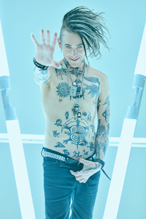 Portrait of a modern expressive punk rock musician with cool mohawk posing with bare torso covered...