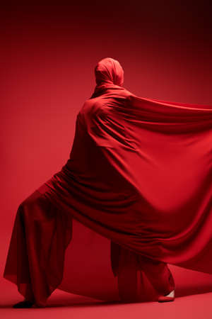 Studio portrait of an expressive female fashion model wrapped in red fabric posing on a red background. High fashion shoot. Full length portrait.の写真素材