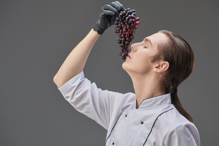 Portrait of a sophisticated  professional young chef in white uniform posing with a delicious bunch...