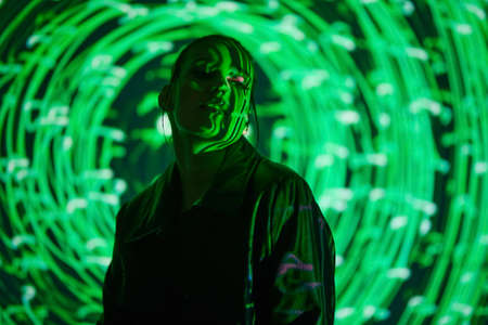 Cyber space and the Matrix concept. Portrait of an attractive confident girl in black leather coat standing in green neon light circles. Future technologies. Beauty and fashion.の写真素材