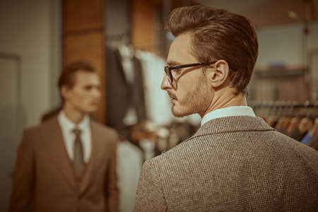 Portrait of a well-groomed brunette man in an elegant classic suit, standing with his back to the camera in a men's clothing store. Men's fashion, respectable style.の写真素材