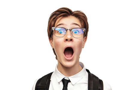 Portrait of an emotional smart teen boy in school uniform and glasses looking at camera with big surprise and screaming out loud. Studio shot on a white background.の写真素材