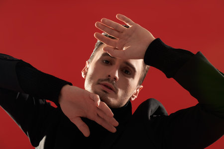 Studio shot of an expressive handsome young man in stylish black clothes posing on a red background. Men's fashion and beauty.の写真素材
