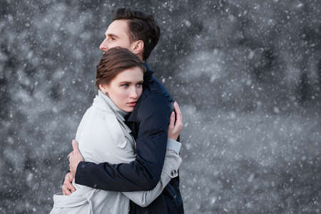 People in love. Portrait of a beautiful young loving couple in stylish clothes hugging each other on a snowy winter background. Copy space.の写真素材