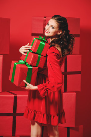 Happy girl with evening makeup and hairstyle wearing a nice red dress happily carries a pile of...