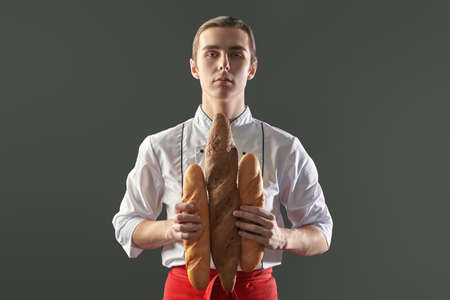 Young professional male chef poses on the grey background with different types of baguettes. Food and meals.の写真素材
