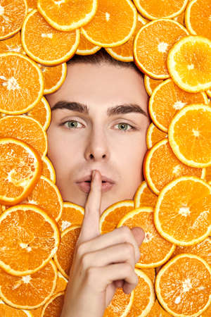 Fresh fruits and juices. Vitamins. Close-up shot of a handsome young male chef's face, laid by oranges holding his finger on his lips as a silence gesture.の写真素材