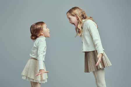 Portrait of two little sisters in light classic clothes scream at each other during their quarrel. Family relationship. Sibling interaction problems.の写真素材
