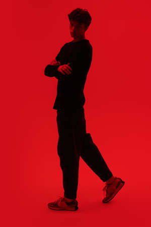 Full legth shot of a handsome guy with a sad look on his face standing on a bright red background hugging himself. Young people and mental health.の写真素材