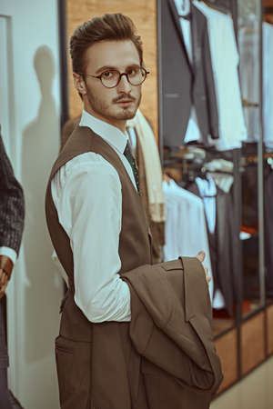 Portrait of an attractive young brunet man dressed in a smart brown three-piece suit standing in a men's clothing store and looking at the camera. Men's business fashion.の写真素材