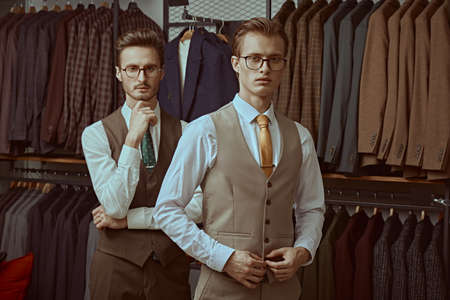 Men's fashion. Two well-groomed successful businessmen in elegant classic suits and glasses stand in a premium men's clothing store.の写真素材