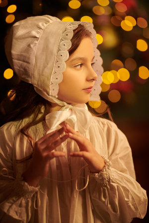On Christmas Eve. The little heroine of an old fairy tale stands in a nightie and a cap, waiting for a miracle on Christmas night. Vintage style.の写真素材