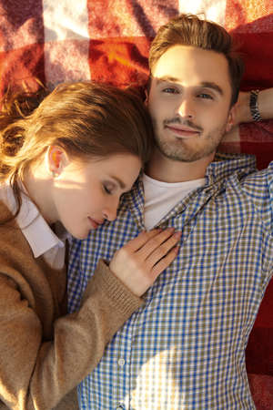 Sweet and tender love. Portrait of a beautiful young couple joyfully lying on the blanket and hugging each other on a wonderful sunny day.の写真素材