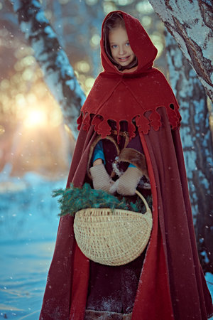 Winter's tale. A cute girl in warm medieval clothes with a cape and a hoodie stands in a snowy...