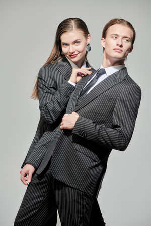 Stylish couple of young people man and woman posing in elegant striped pantsuits. Studio portrait on a gray background. Impeccable look. Fashionable business style.の写真素材