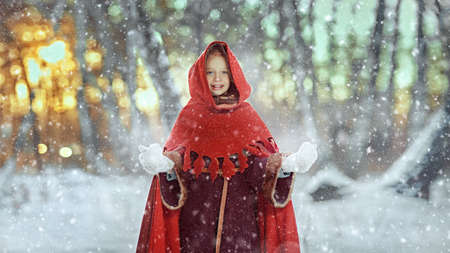A happy girl with blonde hair and clear blue eyes, dressed in medieval winter clothes, stands in a snowy forest at the sunset joyfully smiling. Fairy tales on Christmas and New Year.の写真素材
