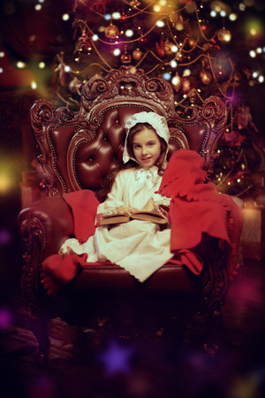 Christmas Fairy Tales. Portrait of a little girl in a nightie and a nightcap, joyfully sitting in a...