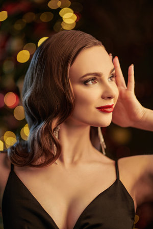 Attractive young woman with evening makeup and hairstyle poses in an elegant black dress on the...