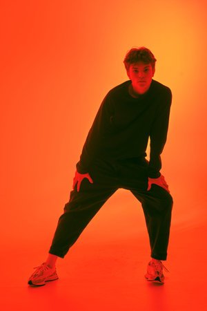 Studio shot of an attractive dark-haired guy in black casual clothes and trainers posing on an...