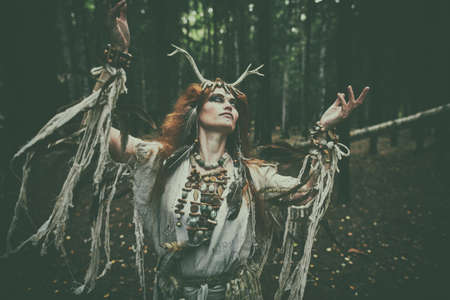 A mystical woman shaman in ethnic dress and deer antlers headdress performs a ritual dance in the forest. Fairy forest witch. Fantasy. Halloween.の写真素材