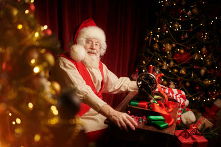 Portrait of joyful Santa Claus sewing Christmas stockings in his workshop. Santa's preparations for Christmas. Workshop of Santa Claus. Christmas traditions and fairy tales.の写真素材