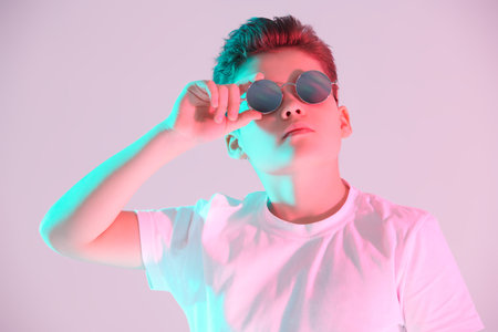 Portrait of a handsome boy teenager in white t-shirt and stylish sunglasses looking up. Studio...