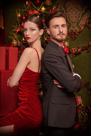 Elegantly dressed young couple pose standing back-to-back among many red gift boxes in expensive interior decorated for Christmas. Christmas and New Year fashion. Holiday sale and shopping concept.の写真素材