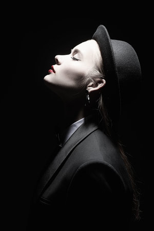 Fashion and art. Elegant fashion model girl in a smart black pantsuit and hat poses in profile with...