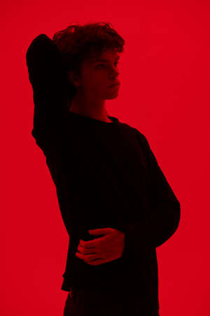 Portrait of a handsome guy with wavy dark hair with a depressed expression on his face standing on a red background looking pensively away. Young people and emotions.の写真素材
