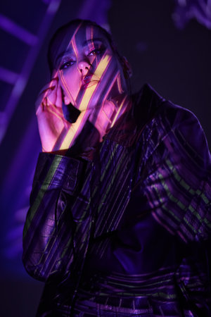 Attractive confident brunette girl in a black leather jacket posing in a dark space with neon beams...