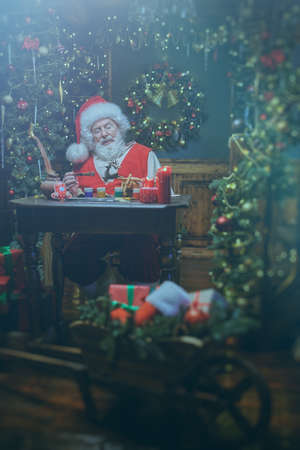 Santa Claus workshop. Portrait of Santa Claus painting toys for gifts to children while being at home, beautifully decorated in honor of Christmas. Christmas and New Year concept.の写真素材