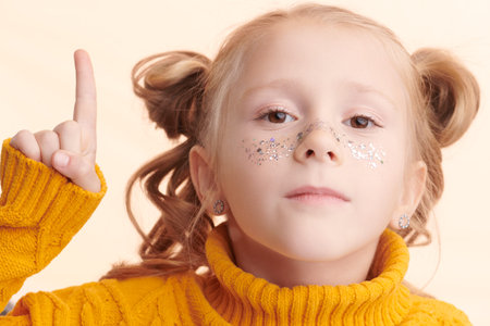A funny little girl with shiny freckles on her face looks at the camera and raises her index finger...