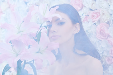 Beauty concept. A beautiful gentle girl stands with lily flowers against a wall with delicate white...