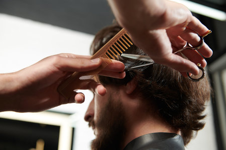 Barbershop. Brunet man getting haircut by a hairdresser while sitting in a chair at barbershop.