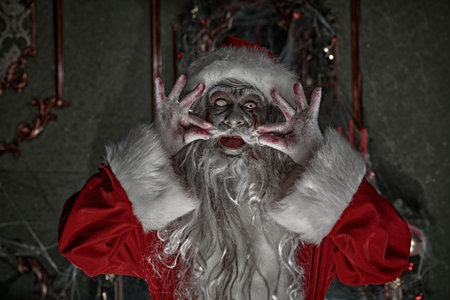 Christmas and Halloween. Scary Zombie Santa Claus stands in a room with a Christmas decoration,...