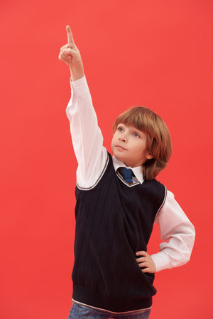 A cute little boy in neat school unifrom points his finger up. Stylish school uniform. Education....
