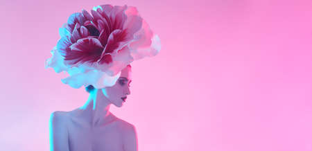beauty concept. Artistic portrait of a beautiful graceful young woman with a large delicate peony flower on her head. Perfume. Makeup and cosmetics. Pink background with copy space.の写真素材