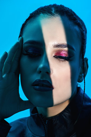 Attractive brunette model with bright makeup posing between light and shadow. Studio shot on a light...