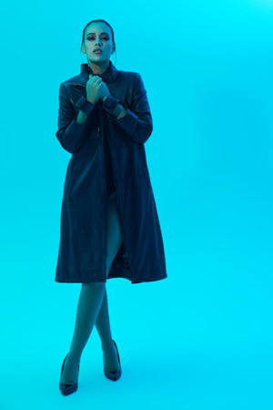 Full length portrait of a beautiful brunette girl model posing in a stylish black leather coat in a blue background. fashion shot.の写真素材