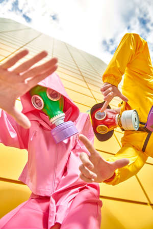 Modern art. A couple of modern young people in bright clothes and gas masks stands by a yellow industrial wall looking at the camera and gesticulating. Stop environmental pollution.の写真素材