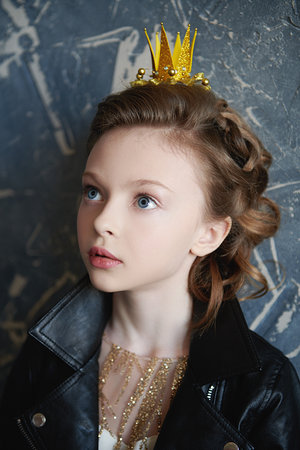 Portrait of a pretty modern little princess girl in a golden dress, black leather jacket and a crown. Dreams and kid's fashion.の写真素材