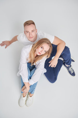 Studio portrait of a beautiful enamored girl and guy sitting next to each other. Full length portrait on a white background. Love concept. Valentine's Day.の写真素材