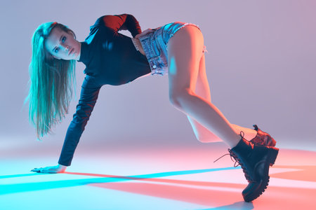 Portrait of an attractive slim girl in black bodysuit and denim shorts performing a modern dance at...