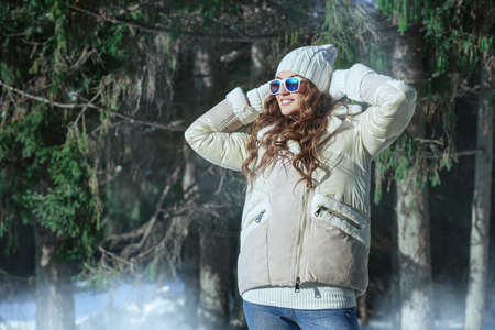 Winter fashion. Portrait of a beautiful girl in fashionable winter clothes, who is standing in a winter park on a sunny day and smiling. Winter activities.の写真素材