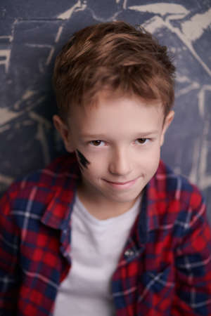 Kids and childhood. A handsome boy with trendy hairstyle who stands in a plaid shirt on a grunge background and smiles.の写真素材