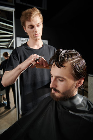 Handsome young man with dark thick hair visits hairdressing salon. Barbershop.