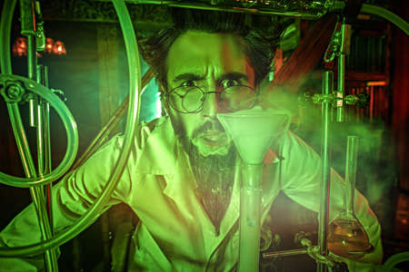A mad scientist, obsessed with his idea, conducts scientific experiments in his laboratory, illuminated by a mysterious green light. Science fiction.の写真素材