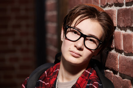 Portrait of a handsome modern teenage boy in glasses, stylish casual clothes and hat leaning wearily...
