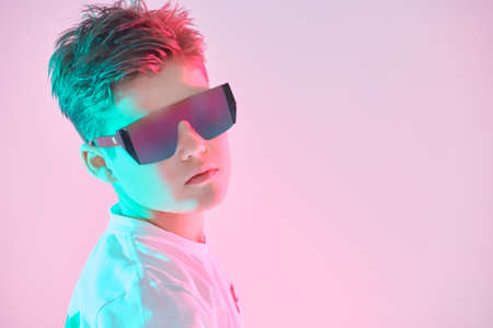 Portrait of a handsome boy teenager in white t-shirt and stylish sunglasses. Studio portrait on a pink background. Children's fashion.の写真素材